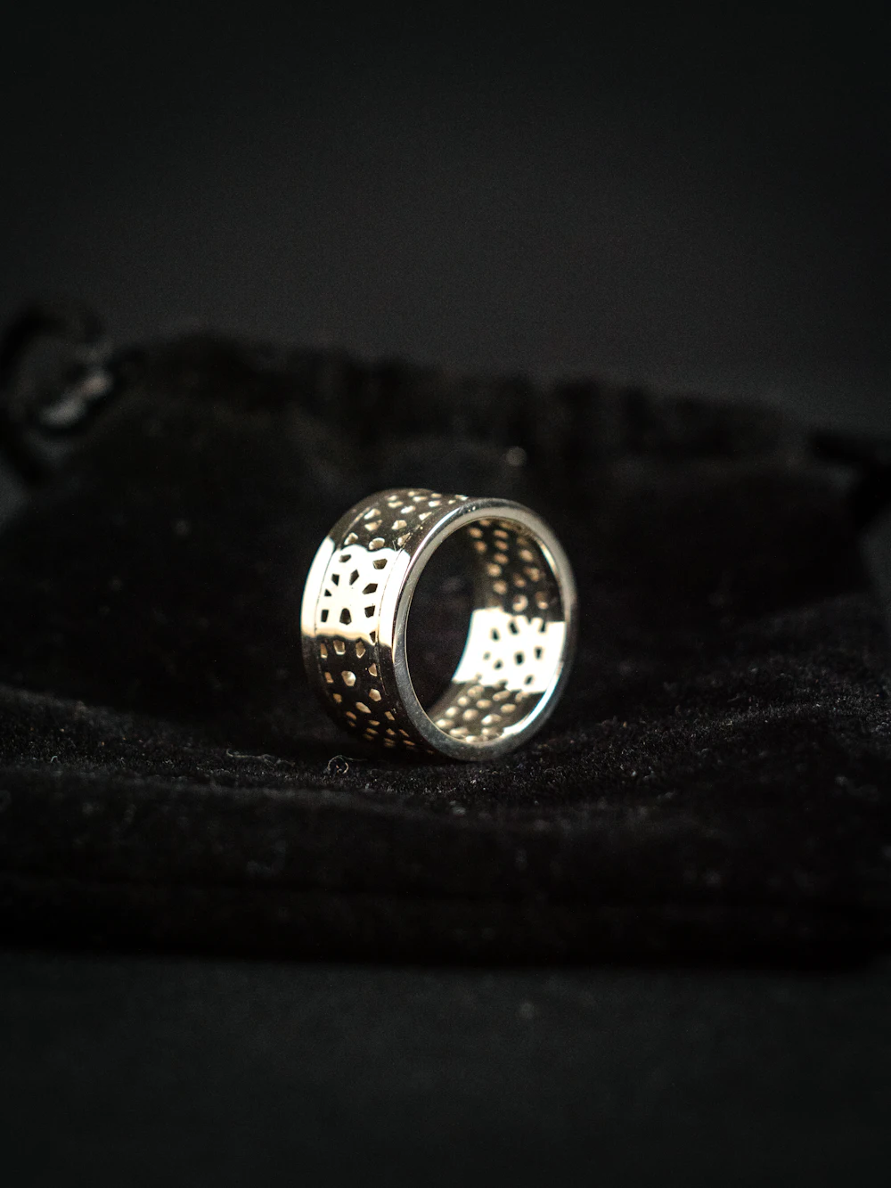 Anillo de plata de banda ancha calada, sobre fondo negro con luz dirigida